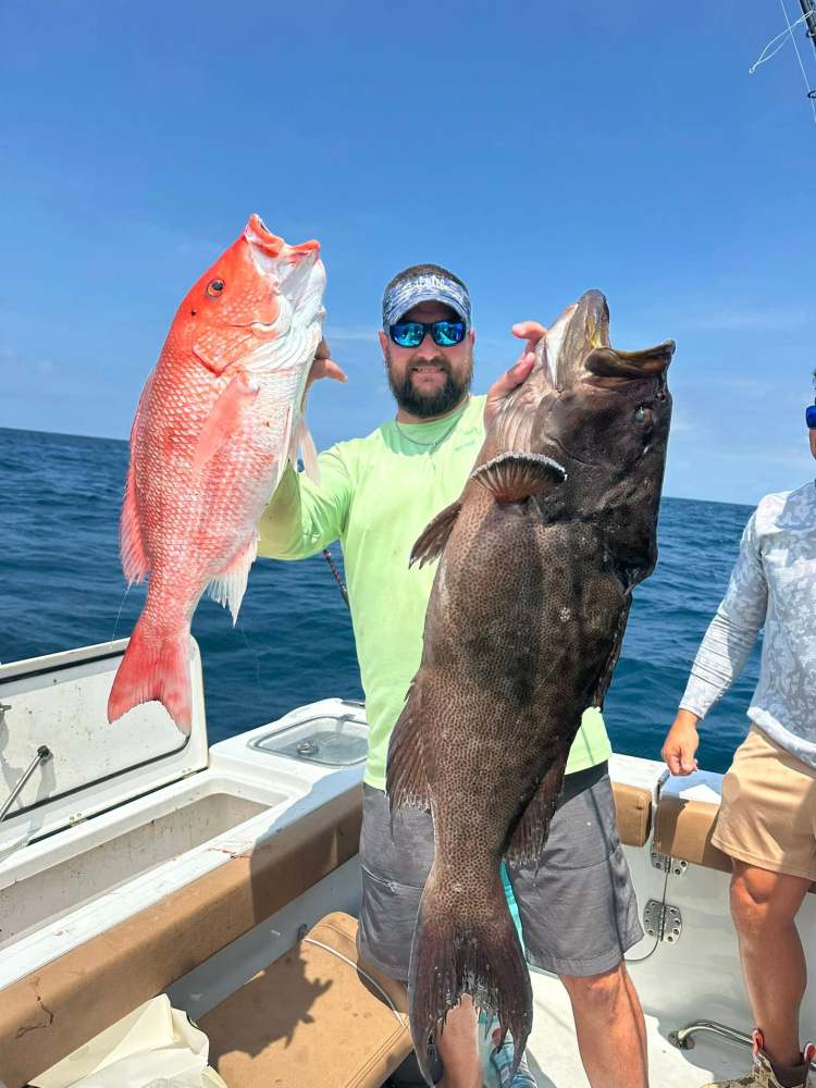 Man on boat holding large red and brown fish under blue sky.