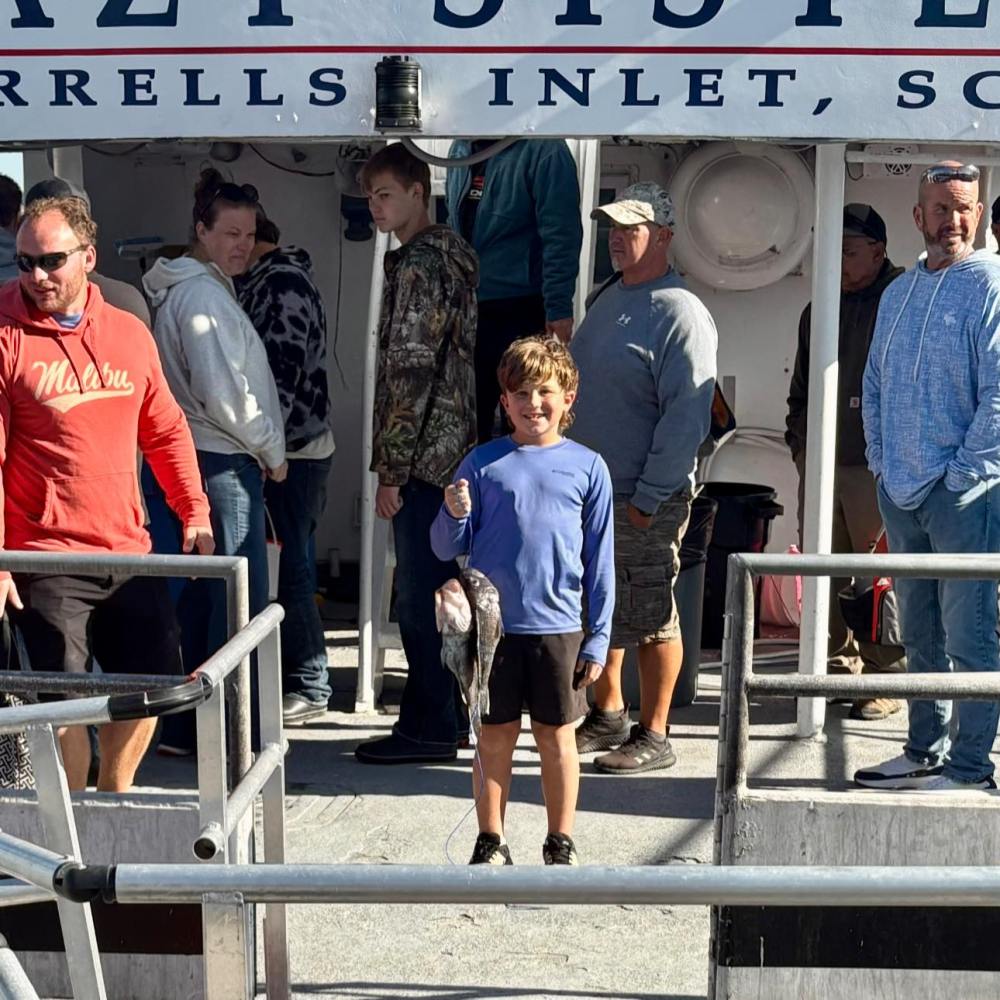 Boy holding a fish, surrounded by adults on a boat.