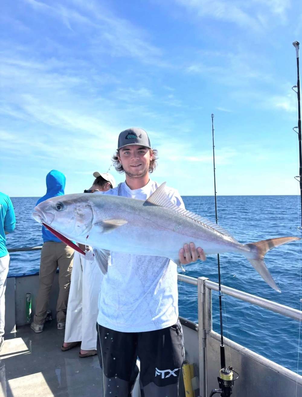 Person on boat holding a large fish with ocean in background.