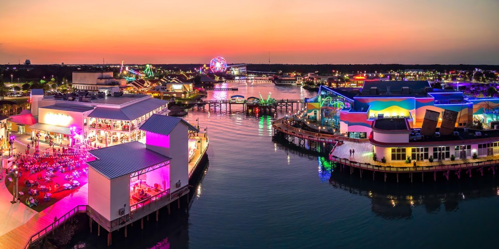 Colorful waterfront amusement park at sunset with vibrant lights.