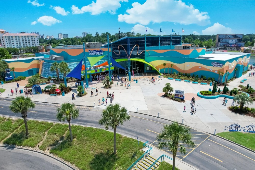 Aerial view of colorful aquarium building with wave patterns and visitors outside.