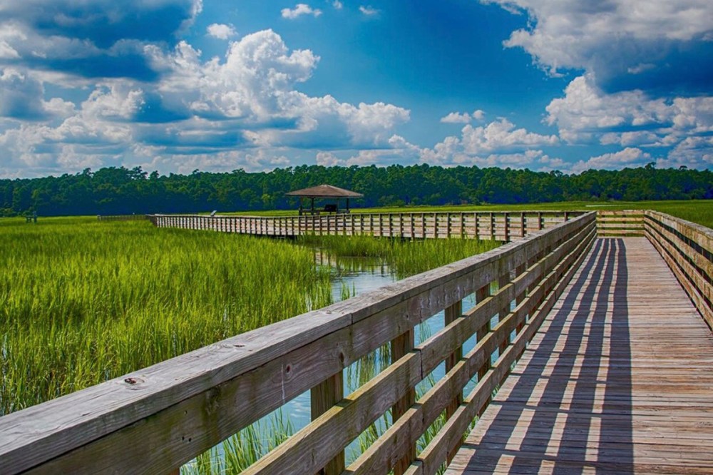 Wooden boardwalk over wetlands with grassy marshes, leading to a gazebo.
