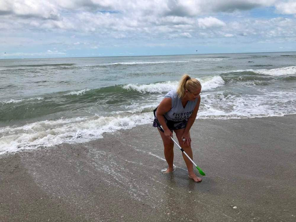 Person using a scoop on a sandy beach by the ocean.